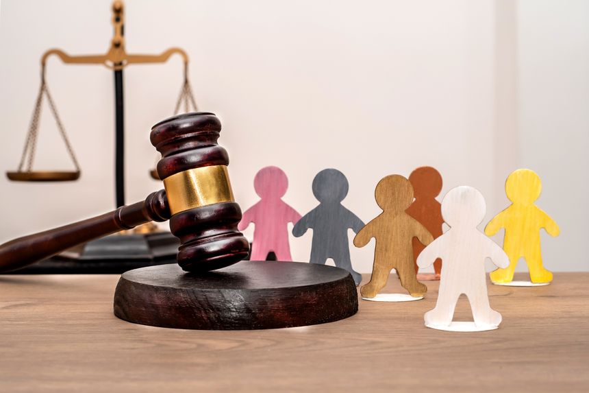 A judge's gavel next to various human figures against a backdrop of the scales of justice. Equality and inclusion before the law.