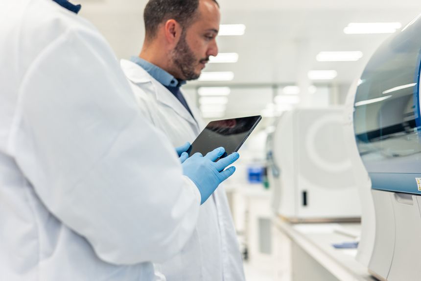 Two scientists wearing lab coats and gloves are using a digital tablet in a modern laboratory, conducting medical research with advanced equipment
