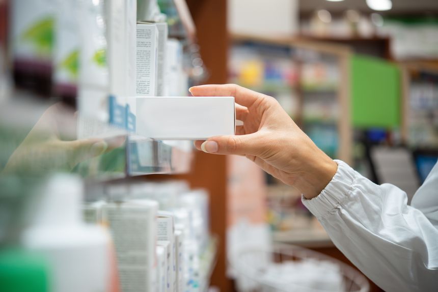 Pharmacist taking medicine box from shelf in a pharmacy