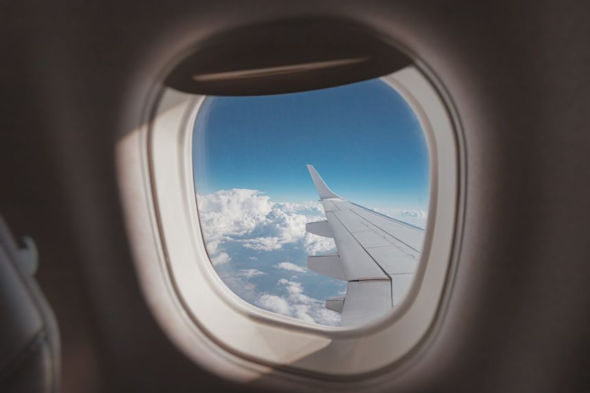 view from the porthole captures a stunning horizon, showcasing the airplane wing against a backdrop of blue skies and fluffy clouds