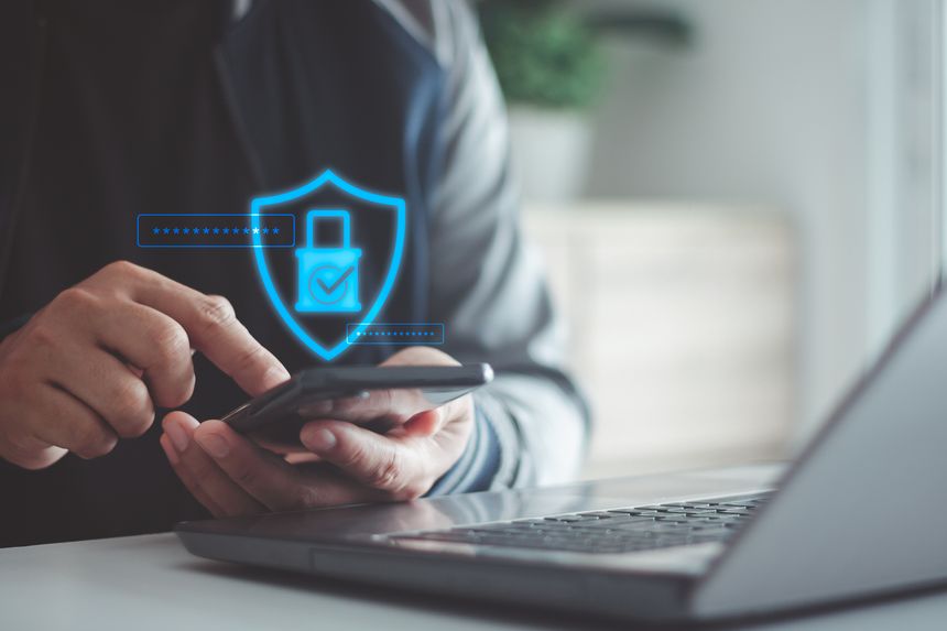 Businessman using smartphone with digital security shield password icon over laptop, cybersecurity, data protection, secure login, mobile authentication, online privacy for modern business technology.