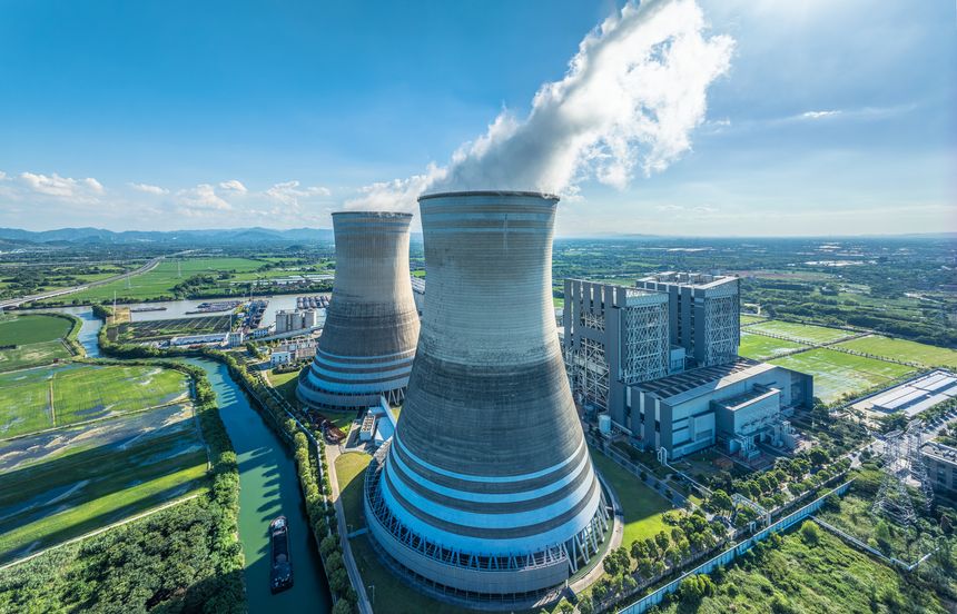 Aerial view captures a power plant with cooling towers and a river landscape, combining energy production with the natural beauty of the surroundings.
