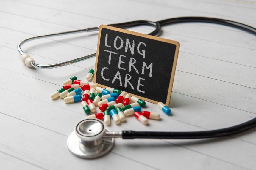 A chalkboard with the words LONG TERM CARE surrounded by scattered pills and a stethoscope. Medical and healthcare concept.