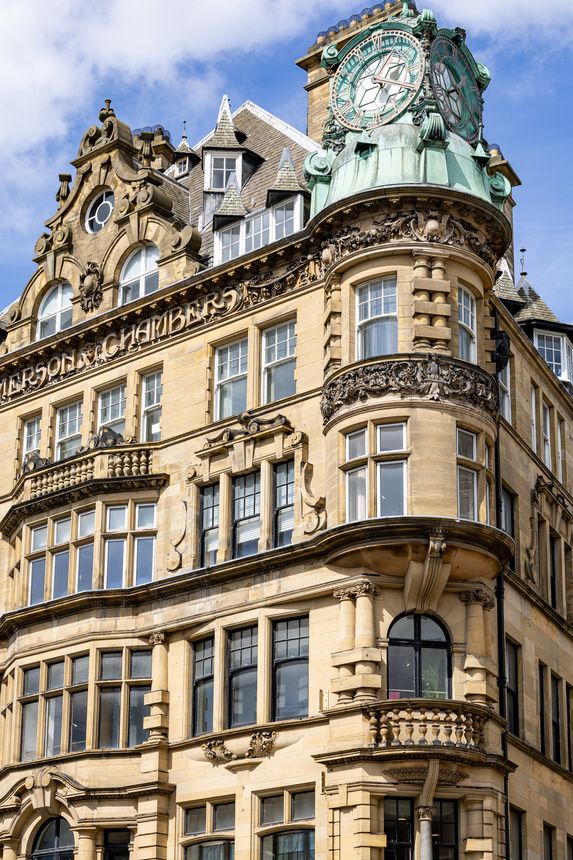 Ornate sandstone building with a prominent green-domed clock tower and arched windows, under a bright blue sky with scattered clouds. Newcastle upon Tyne, UK  - August  10, 2025.