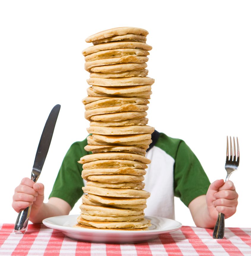 Little boy hidden behind a giant plate of pancakes, with a knife and fork visible on a table cloth. Please see my other photo with a similar theme,