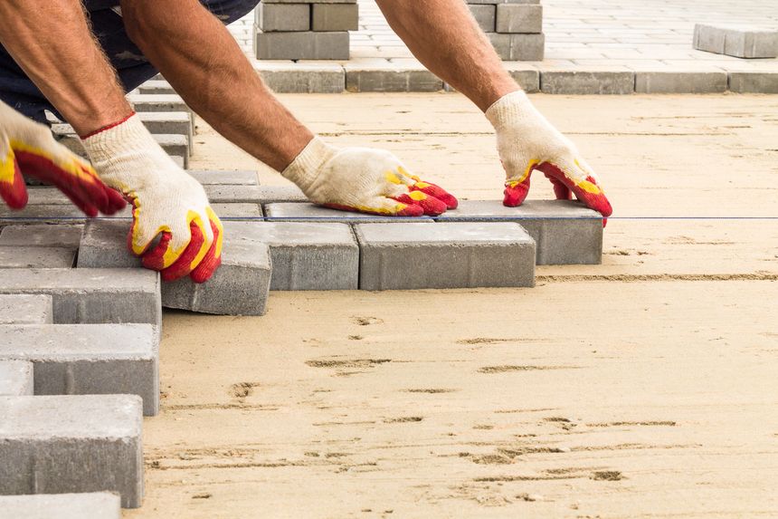 workers lay paving tiles, construction of brick pavement, men's hands in gloves, close up architecture background