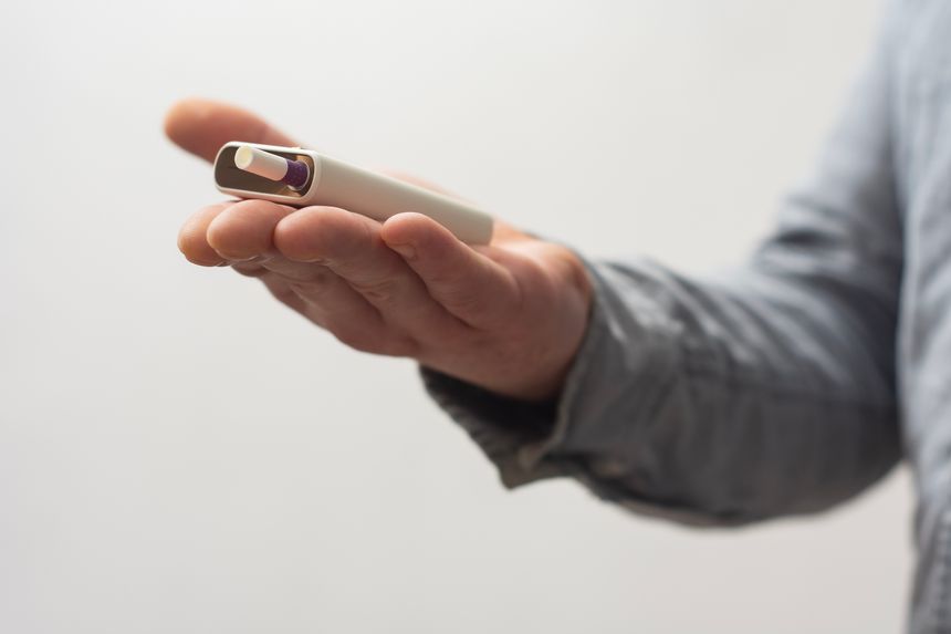 Close-up of a male hand holding a white electronic cigarette with a heated tobacco stick. Photography on a Light Background