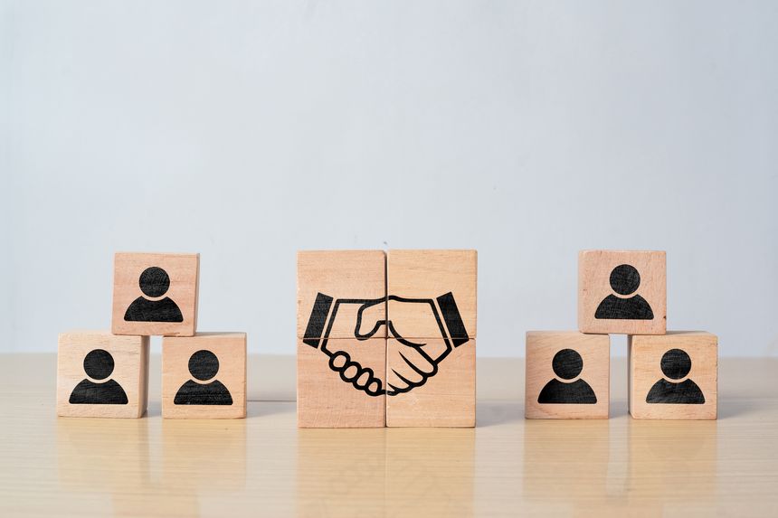 Wooden block with handshake and human icons. Business agreement, partnership, cooperation, and teamwork concept.