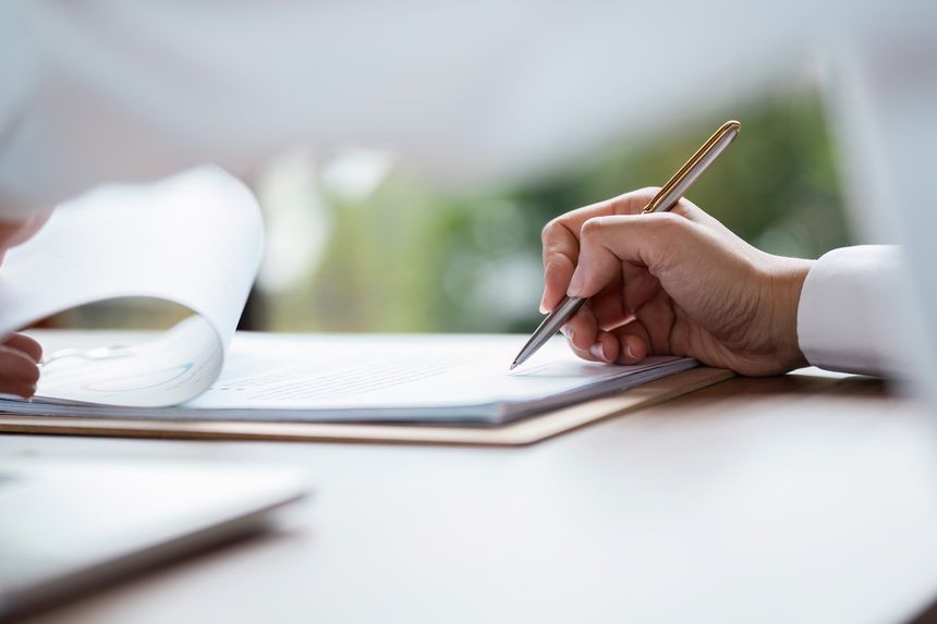 Close-up of a hand signing a business contract with a pen on a desk, symbolizing agreement and professional commitment.