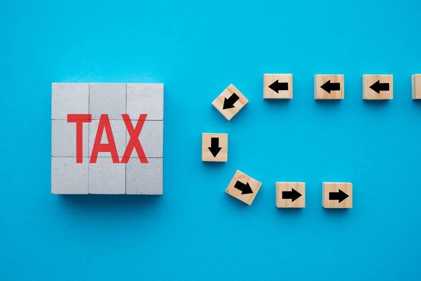 Flat lay of arrow symbol block u-turn avoid TAX word block on blue background. Tax avoidance (minimizing paying) and tax evasion (not paying) concept.