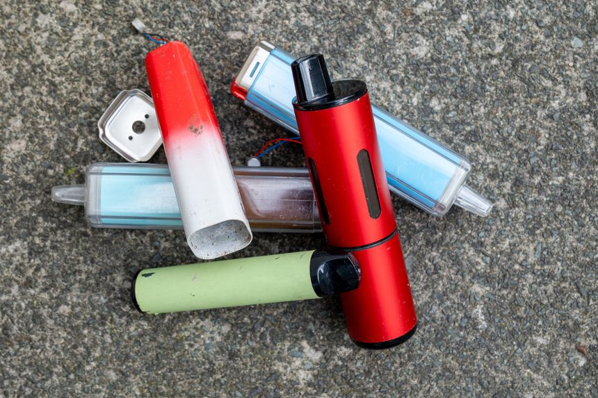 Discarded single use disposable electronic cigarette vapes have been left lying on grey concrete.