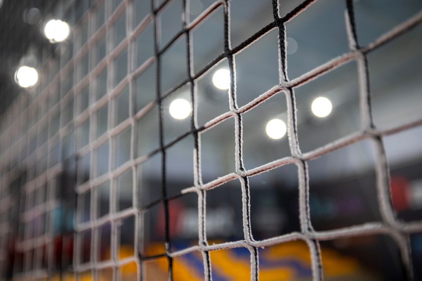 Close-up of a square-patterned black volleyball net with a blurred background showing indistinct colorful shapes and bright lights in an indoor volleyball arena.