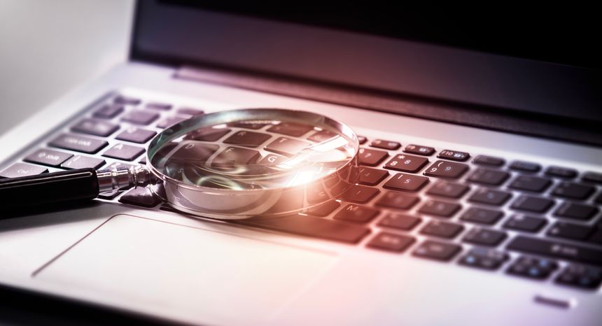 Magnifying glass on laptop keyboard search the internet for online documents background