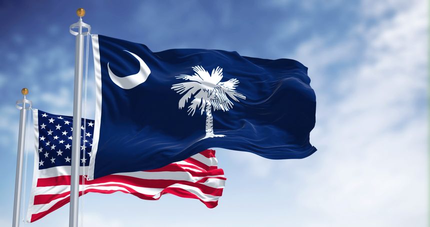 The South Carolina state flag waving along with the national flag of the United States of America. South Carolina is a state in the coastal Southeastern region of the United States