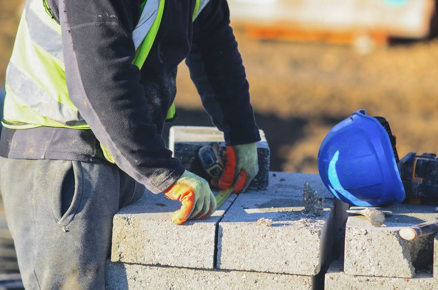 Builder cutting concrete block with chisel and hammer to right size to place it between concrete beams during construction of the beam and block ground floor in the residential house