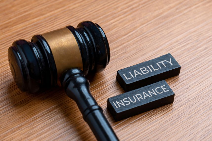 A gavel on a desk next to two stacked wooden blocks with the words LIABILITY INSURANCE. Law concept.