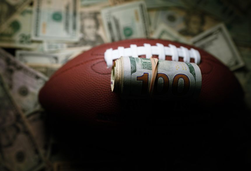 Rolled hundred dollar bills on a football, with cash background