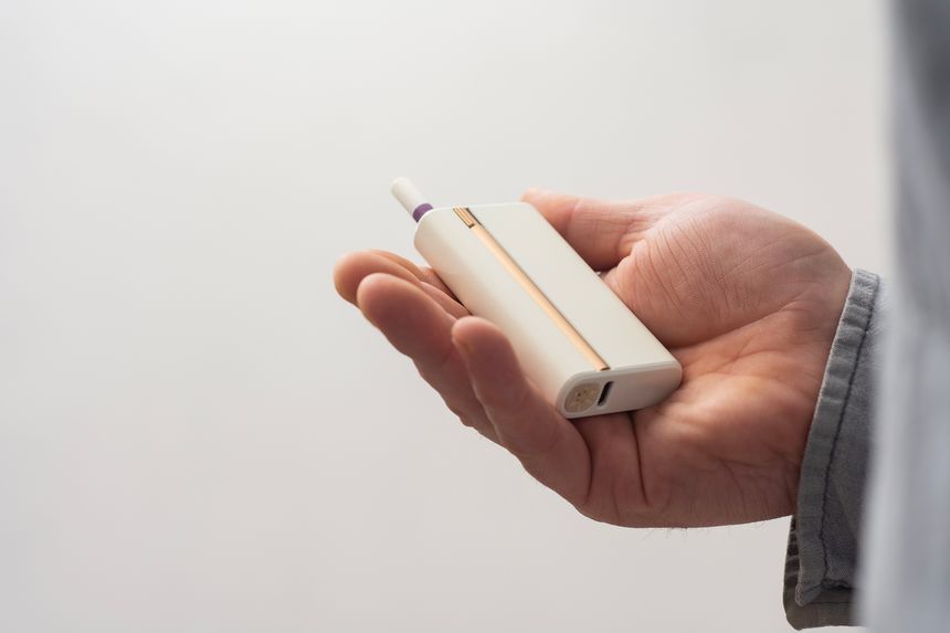 Close-up of a male hand holding a white electronic cigarette with a heated tobacco stick. Photography on a Light Background