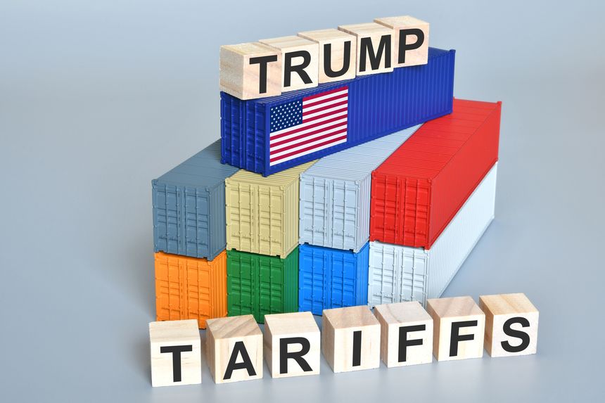 Wood cubes with Trump Tariffs words over containers with flag of US. Concetto per le nuove tariffe imposte dal Presidente degli Stati Uniti Donald Trump.