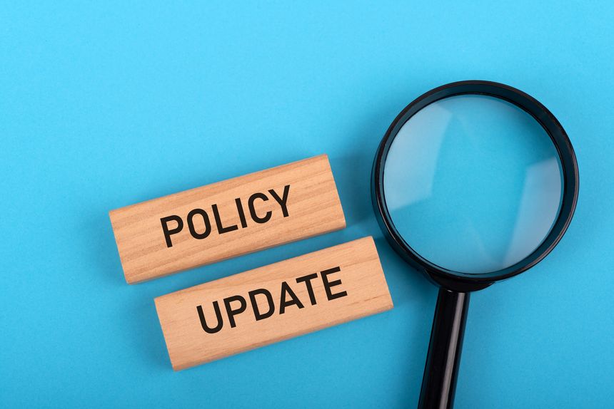 Magnifying glass and policy update text on wood block on blue background
