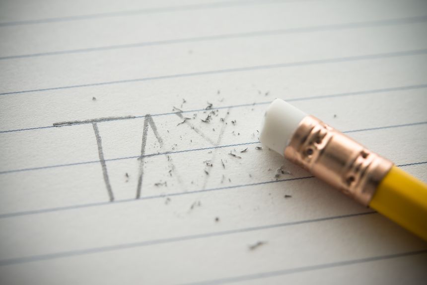 Close up handwriting TAX is erased via pencil eraser on notepad background. Tax avoidance (minimizing paying) and tax evasion (not paying), business, finance and investment concept.