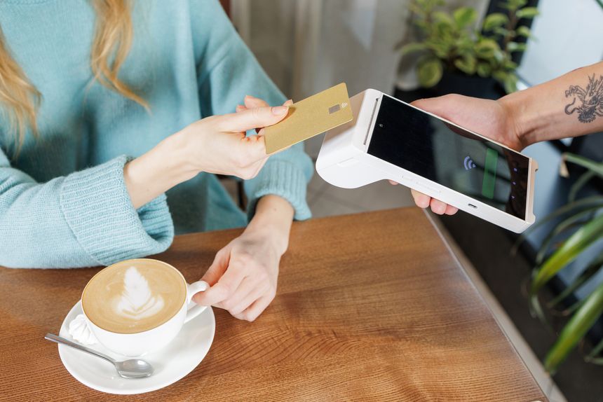 Customer pays for coffee using NFC bank card on handheld POS terminal during tableside checkout in cafe contactless payment technology