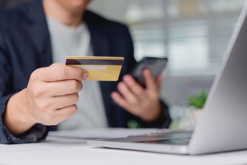 Customer verifies online purchase with credit card and smartphone at office desk near laptop, mobile payment ecommerce banking secure transaction convenience concept