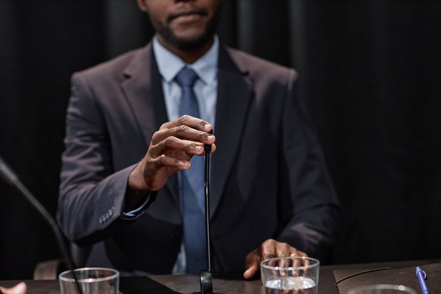Cropped shot of African American politician adjusting microphone giving public speech on law reforms while sitting at meeting table during press conference, copy space