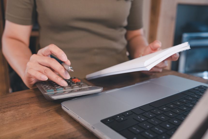 Woman calculating expenses with calculator, laptop, and documents at home office, managing finance, budgeting, online business, accounting, and personal financial planning