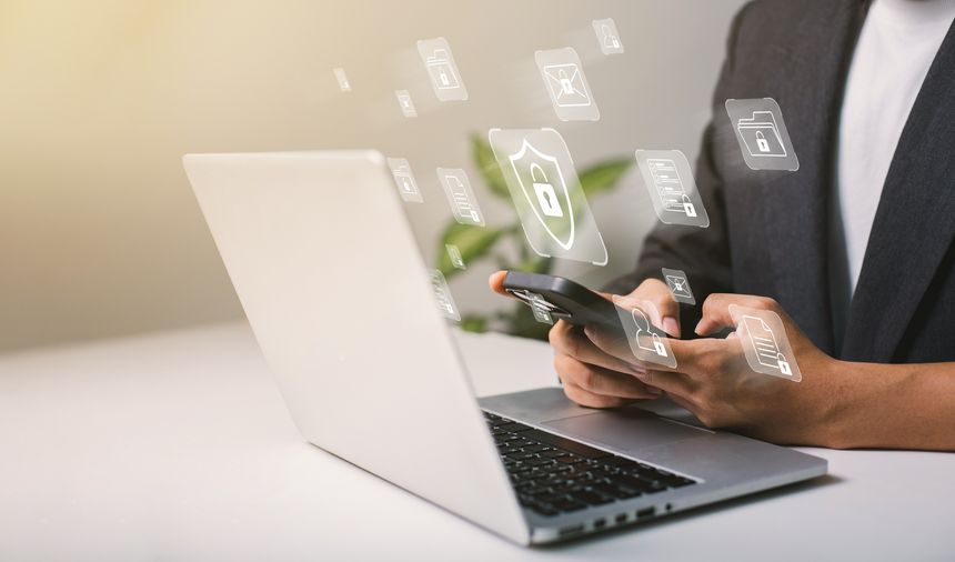 A businessman works on his laptop at home with a virtual display showing a symbol to signify cyber security privacy and online data protection.
