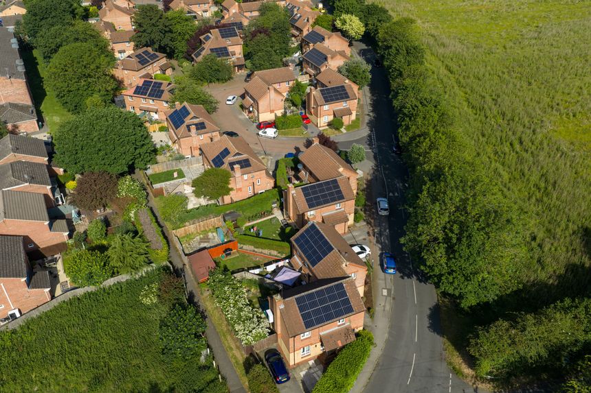 Drone view of residential homes with rooftop solar panels in Selby North Yorkshire bordered by countryside fields and mature trees showing sustainable housing and renewable energy adoption