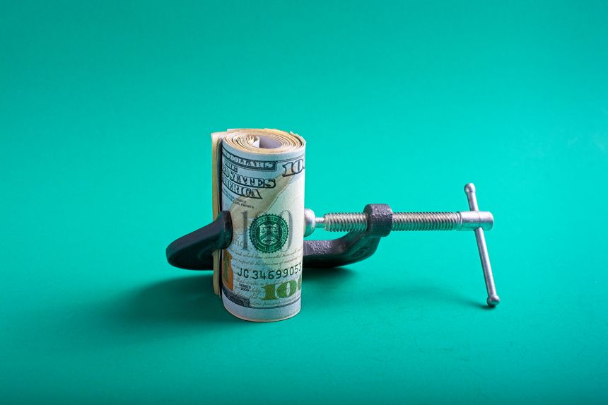 Money squeeze concept of inflation with roll of U.S. currency  compressed between jaws of a c-clamp