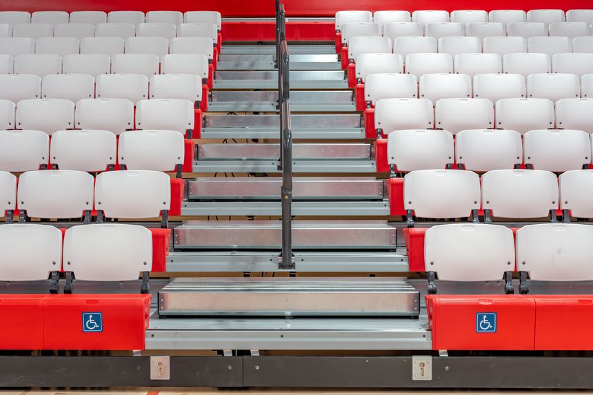 Accessible symbol on the front row of red and white plastic interior gymnasium bleachers.