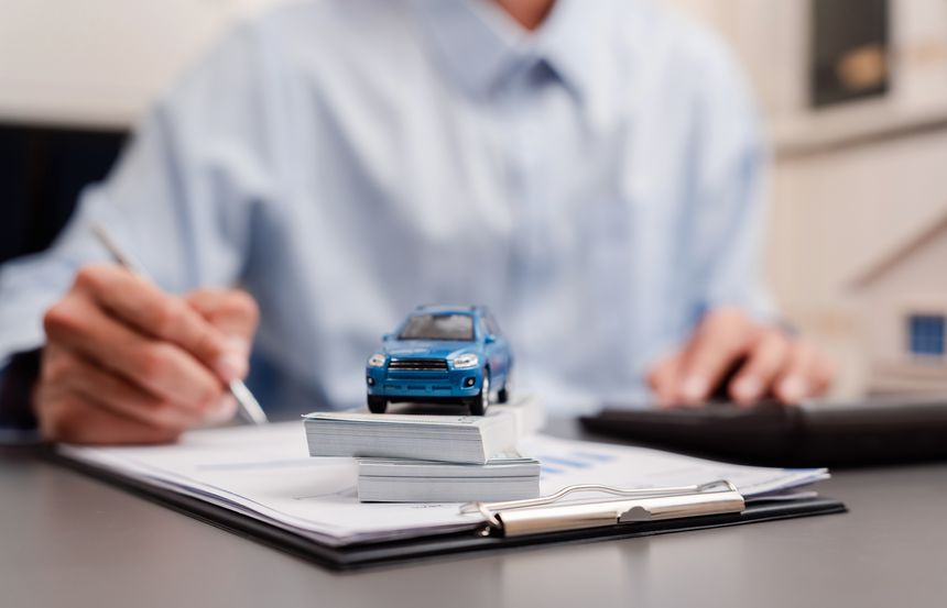 Auto loan agreement and car purchase concept. Man signing contract with toy car and money cash on desk.