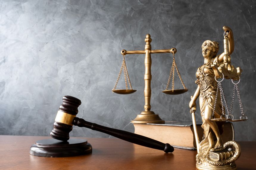 Golden Lady Justice statue, judge gavel, and balanced scales on a law book with gray background, representing fairness, legal authority, courtroom judgment, and professional law concept.