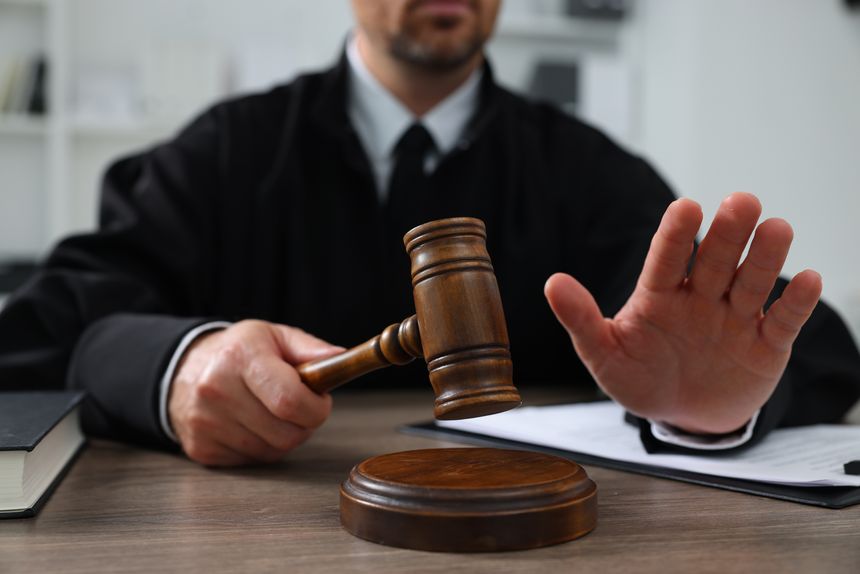 Judge with gavel and papers sitting at wooden table indoors, closeup