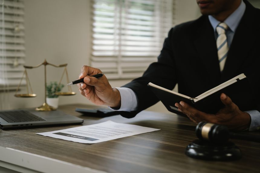 Close-up of a legal gavel on a wooden desk as a lawyer reviews documents beside a laptop, representing law, justice, legal services, court proceedings, and professional legal consultation.