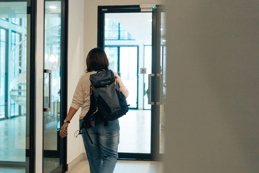 Woman walking away with a backpack, moving through a modern architectural interior