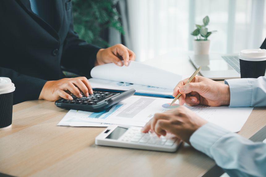 Business partners using calculators and analyzing financial chart reports during a corporate meeting. Professional accountants working together on budget planning and investment analysis.