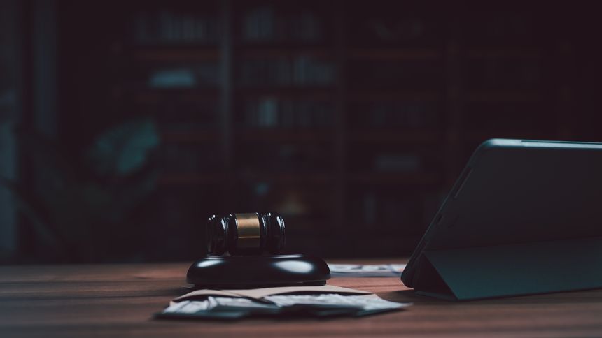 Legal gavel, cash currency bills, and digital tablet displayed upon dark wooden table inside law office, symbolizing justice, crime investigation, trial procedures, and financial fraud litigation.