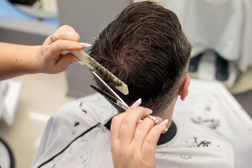 Close up of a barber holding scissors and a comb while cutting a man hair, precise hair trimming technique performed on the back of the head in a professional hair barbershop setting during a haircut session