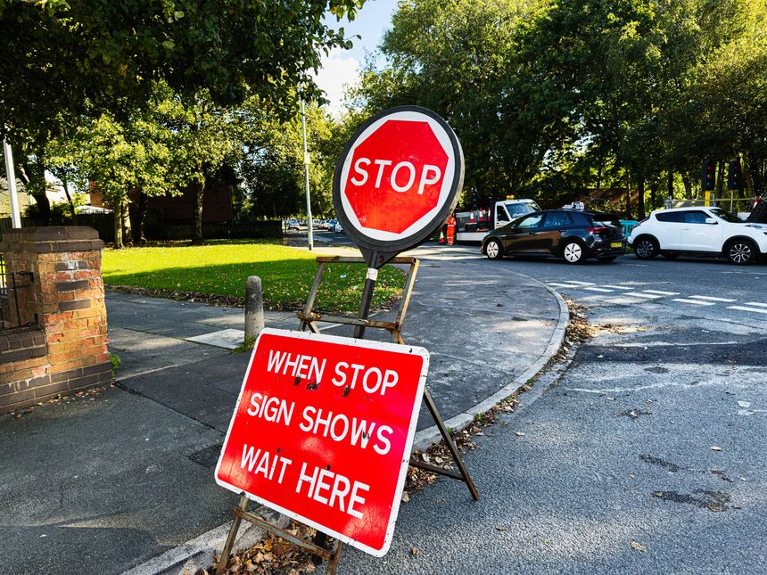 A stop sign and red instruction board on a calm Manchester street corner.