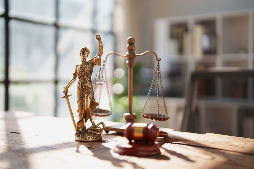 Lady Justice statue on a wooden desk with scales and sword beside a gavel, symbolizing fairness, rule of law and the judicial process in a law office setting