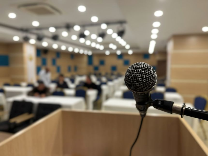 A microphone on a podium and a conference hall waiting in the blurred background. Presentation, speech, and event themes.