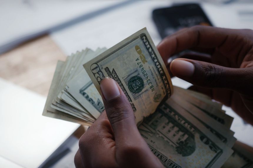 Close-up of hands counting US dollar banknotes on a desk, illustrating cash payment, savings, budgeting, and personal finance themes. Clean, natural light scene with anonymous subject, ideal for banking, money management, or economy concepts.