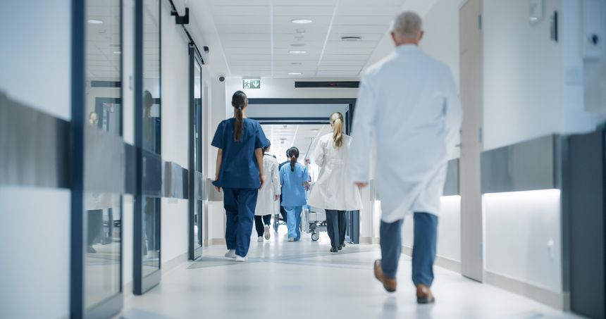 Hospital Hallway with Doctors, Nurses and Specialists in Hospital. Female and Male Physicians, Surgeons, Healthcare Officials Walk Together in Corridor with Their Back to Camera