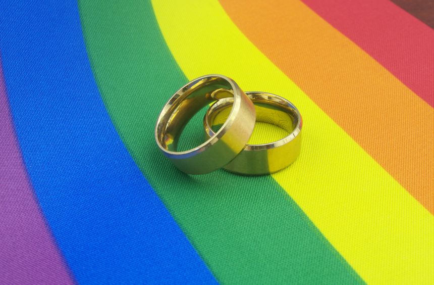 Gold wedding rings on LGBT pride flag. LGBT marriage concept.