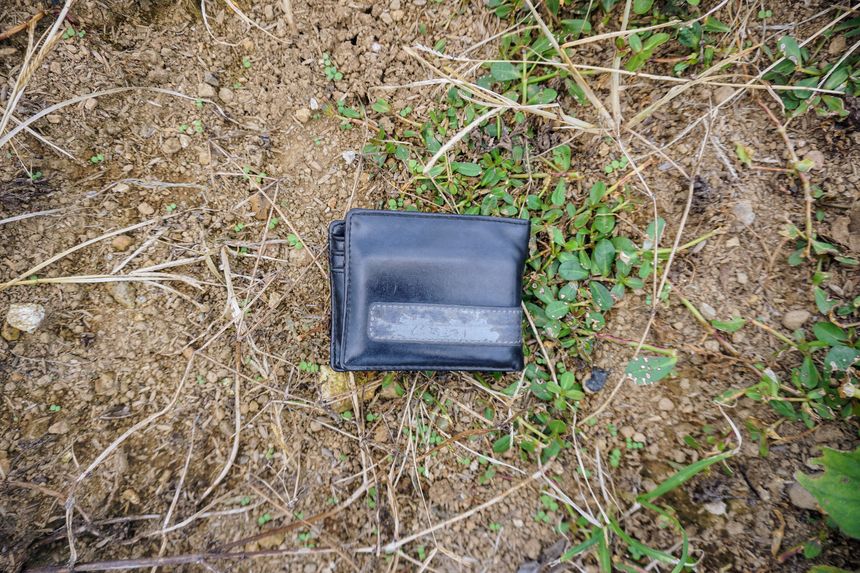 A lost black leather wallet lying abandoned on dry, grassy ground.
