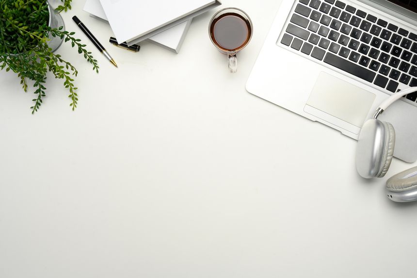 Minimalist workspace with laptop, coffee cup, headphones and notebooks on white desk.