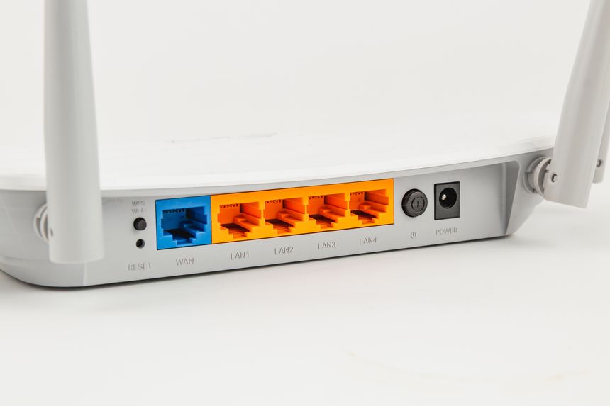 The back of a wireless router shows various Ethernet ports and a power connection. The device is designed for home networking and internet access.